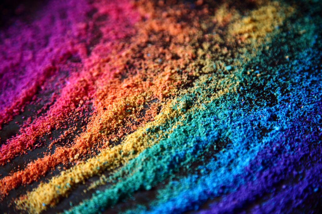 Close-up of colorful powder arranged in diagonal stripes, creating a vibrant rainbow gradient from pink and red to blue and purple.