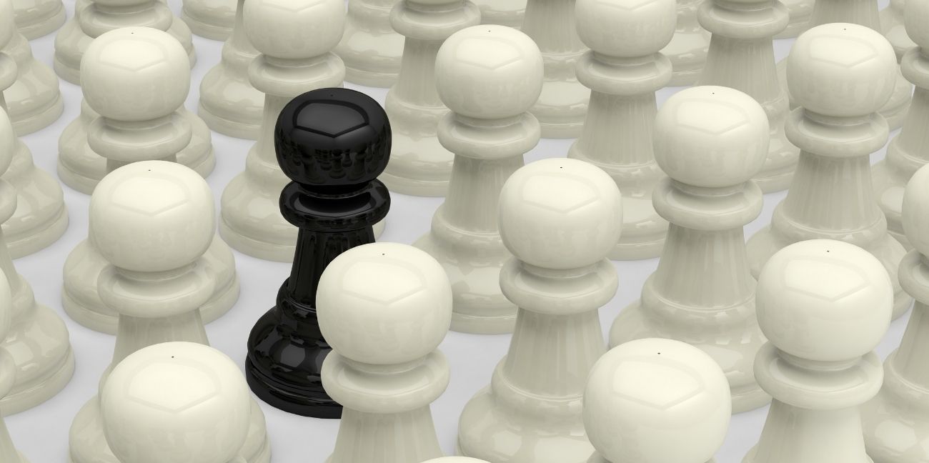 A lone black chess piece among white pieces.