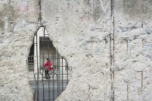 Cyclist in red framed by a broken concrete wall, illustrating the themes of intersectionality and holistic data collection.