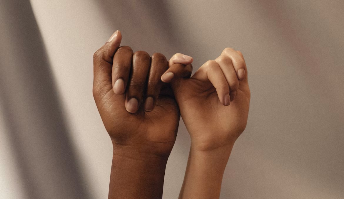 Two hands with different skin shades linking pinkies